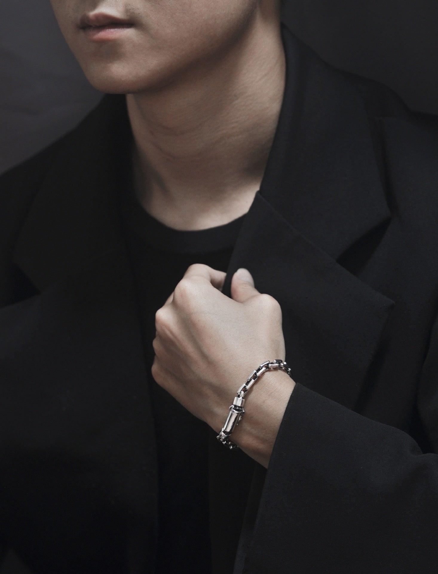 Person wearing a black coat and bracelet, with a dark background