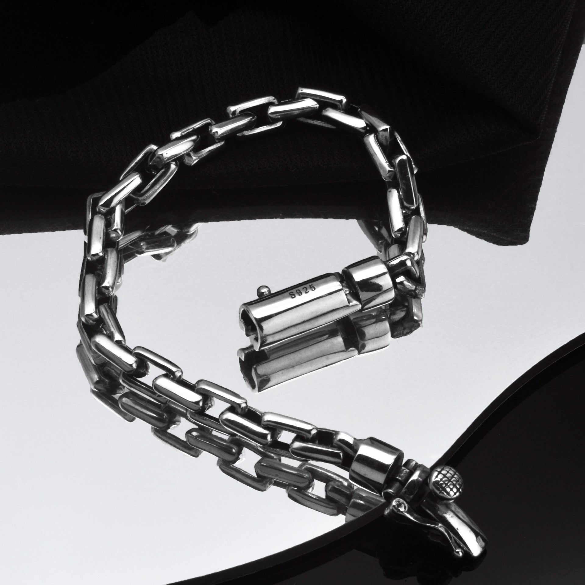 Silver chain bracelet on a reflective surface with a dark background