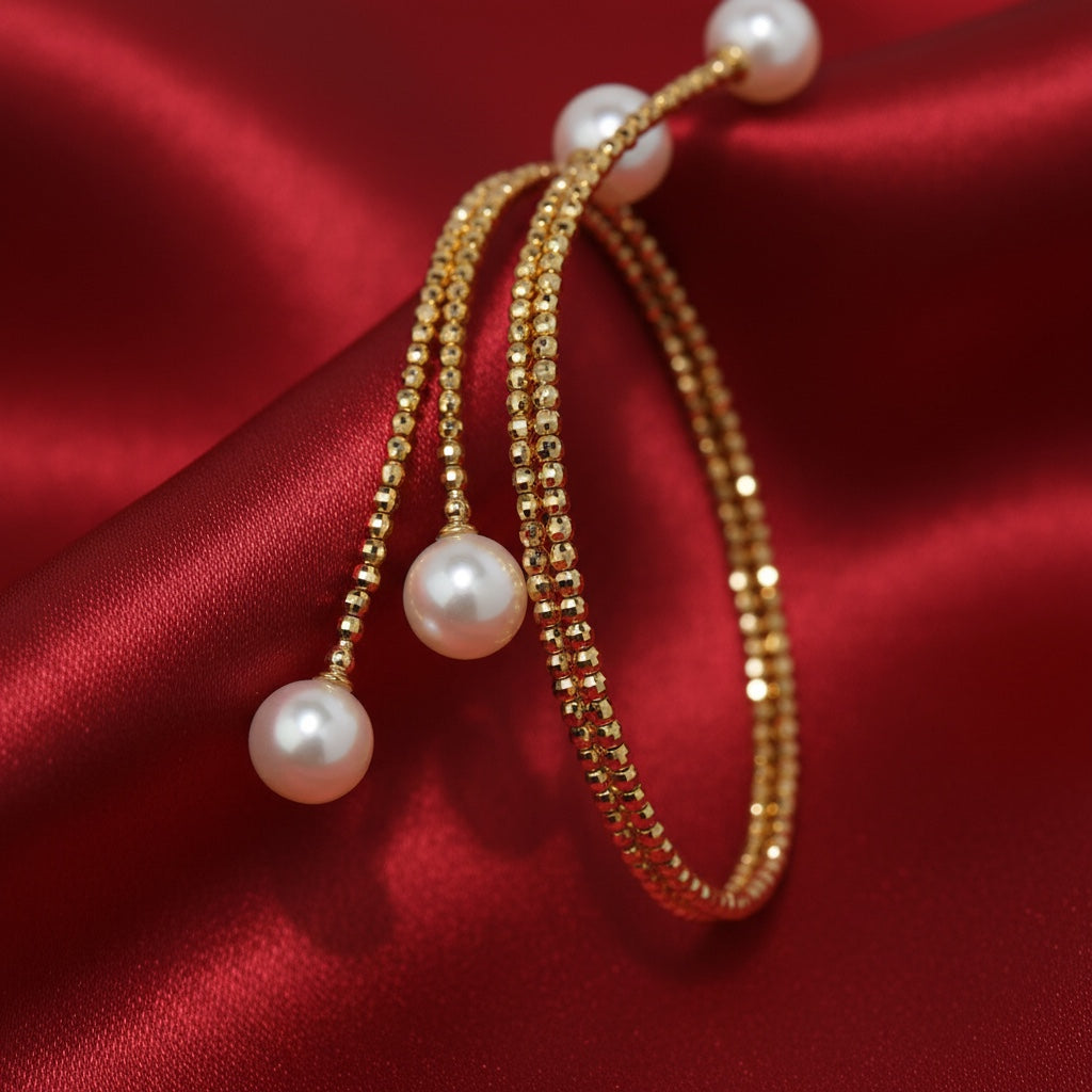 BoxUnboxed 18K yellow gold spiral bangle with diamond-cut beads and three Akoya pearls. Flexible cuff design.