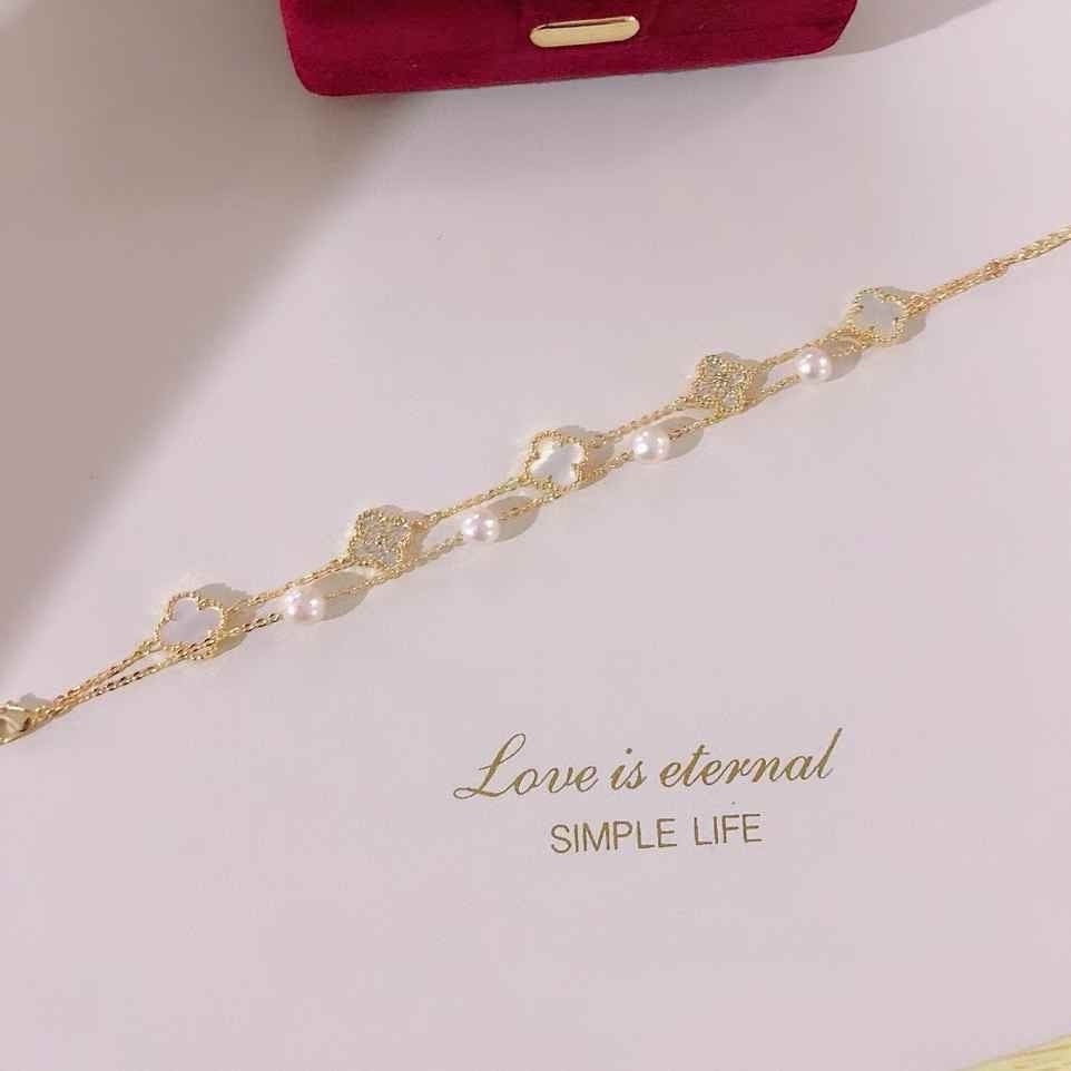 BoxUnboxed double-layer bracelet with white pearls and gold clover charms. Features a gold-plated finish and hypoallergenic design.