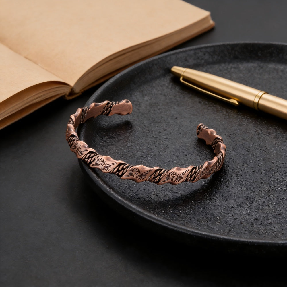 BoxUnboxed Helix Grounding Cuff made of 99.99% pure twisted copper with geometric sun patterns on a black plate.